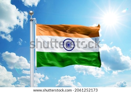 National India flag waving in the wind, against the blue sky. Wavy flag in the sky with sunbeams.