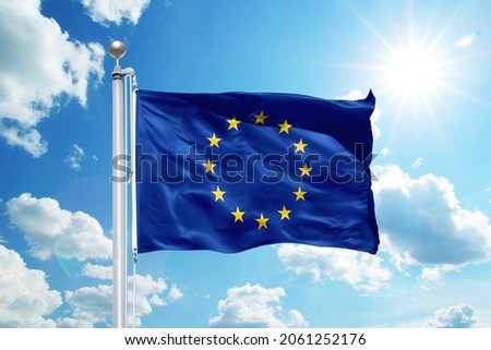 National Europe flag waving in the wind, against the blue sky. Wavy flag in the sky with sunbeams. Royalty-Free Stock Photo #2061252176