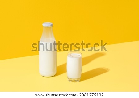 Glass and bottle with fresh milk in bright light on a yellow table. Milk in glass bottle minimalist on a colorful background