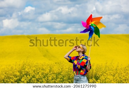 Beautiful female in 90s stylish shirt with pinwheel in rapeseed field Royalty-Free Stock Photo #2061275990