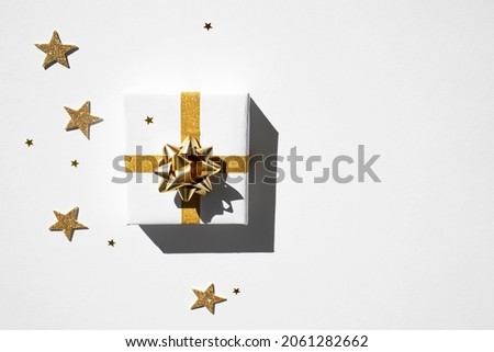 A box with a Christmas present in white paper with a gold bow on a white background. Top view, place for text.