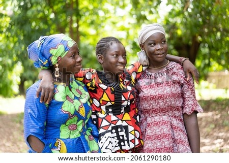 Three beautiful black African adolescent girls in colourful traditional outfit embracing each other; friendship concept Royalty-Free Stock Photo #2061290180