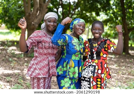 Group of young black African villagers in colourful traditional dresses smiling at the camera with their clenched fists as a symbol for women's strength and gender equality Royalty-Free Stock Photo #2061290198