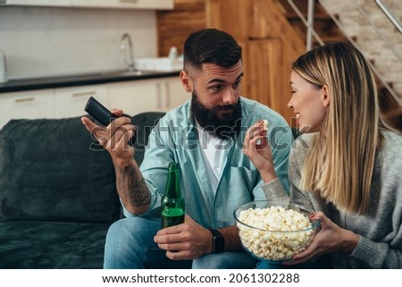 Beautiful young couple drinking beer and watching television together at home