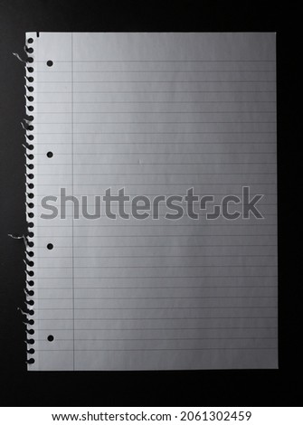 Hole punched sheet of lined white notebook paper, torn from spiral binding, on black background. monochrome light and texture, abstract background image. Royalty-Free Stock Photo #2061302459
