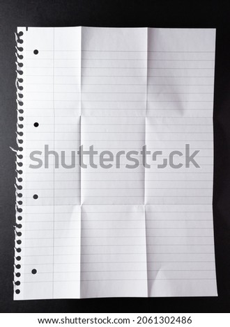 Hole punched sheet of lined paper, torn from spiral binding, folded into nine equal parts, on black. monochrome light and texture, abstract background image. Royalty-Free Stock Photo #2061302486