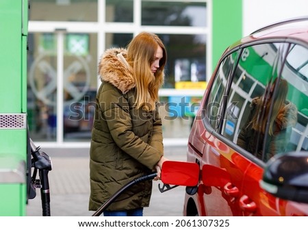 Young caucasian woman at self-service gas station, hold fuel nozzle and refuel the car with petrol, diesel, gas. Pretty woman filling her auto with gasoline or benzine, outdoors. Self service gas pump Royalty-Free Stock Photo #2061307325