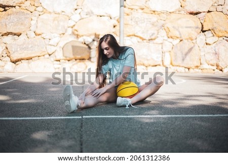 a pretty young girl posing with a basketball on an outdoor court.