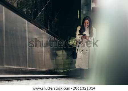 Beautiful young woman using a smartphone and riding the escalator in the subway Royalty-Free Stock Photo #2061321314