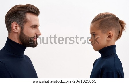 Side view young Caucasian dad and teen son on white studio background face each other. Father and small little teenage boy child look in eyes, two male generations picture. Family unity concept.