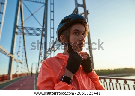 Sporty millennial gen z female cyclist wear helmet before bike riding training outdoors. Active young Caucasian woman in sportswear head-piece armor do sports cycle skate exercise outside. Royalty-Free Stock Photo #2061323441