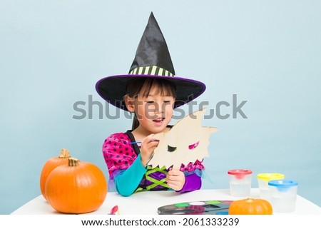 young girl painting halloween costume mask against blue background