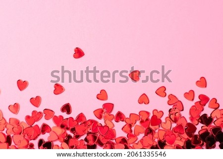 Red confetti in the form of hearts on a pink background. Valentines day backdrop. Flat lay style with minimalistic design. Template for banner or party invitation