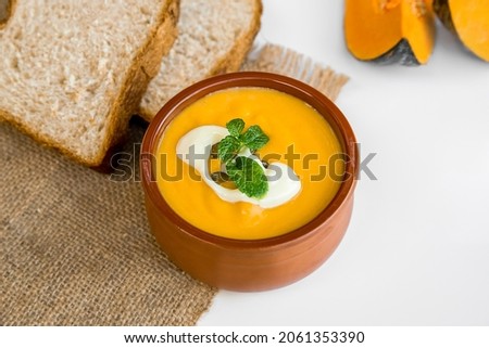 yellow pumpkin soup served and ready with bread, two pieces of raw pumkin in the background, thanksgiving or winter meal, traditional autumn food. 