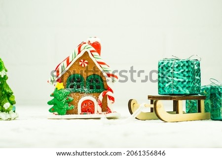 A toy ginger house next to a sleigh full of Christmas gifts. New year card and holiday design with copy space.