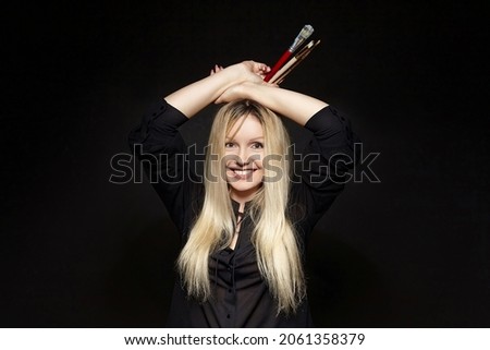 young blonde artist with a smile holding a brush in her hand. photo shoot on a black background in the studio.