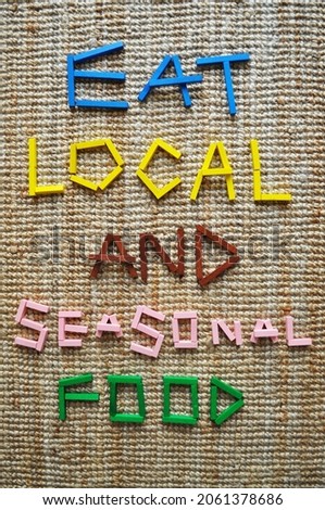 3D text in wooden bricks on jute carpet. It reads Eat Local And Seasonal Food. Message for sustainability, climate change mitigation, climate action, carbon footprint reduction, lower CO2 emissions. Royalty-Free Stock Photo #2061378686