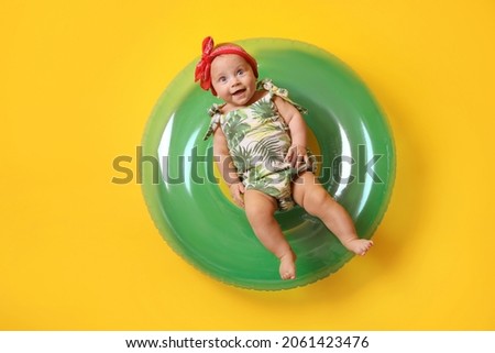 Cute little baby in headband with inflatable ring on yellow background
