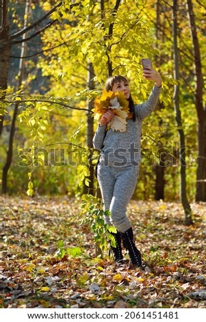 Beautiful girl takes selfi on the phone in the autumn park