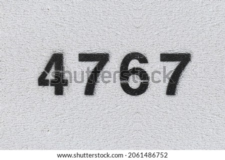 Black Number 4767 on the white wall. Spray paint. Number four thousand seven hundred and sixty seven.