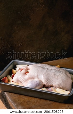 Raw organic uncooked young whole duck with sliced apples in baking tray standing on wooden table. Copy space