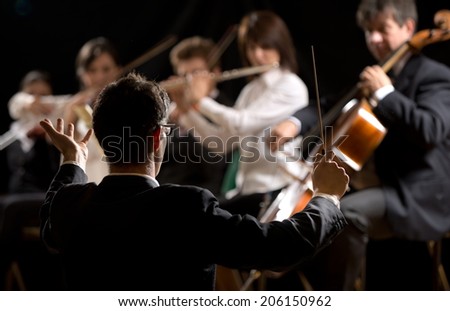 Conductor directing symphony orchestra with performers on background. Royalty-Free Stock Photo #206150962