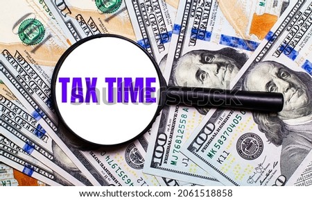Background with dollar bills under a magnifying glass with the text TAX TIME. Financial concept