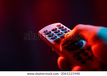 Hold remote control in hand and zap. Male hand is holding TV remote control, streaming on a smart TV. Royalty-Free Stock Photo #2061521948