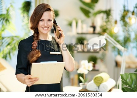 happy female employee with clipboard talking on a smartphone in modern beauty salon. Royalty-Free Stock Photo #2061530354