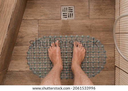 Men's feet stand on a plastic anti-slip mat next to the floor drain in the bathroom or shower. Royalty-Free Stock Photo #2061533996