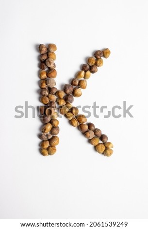 Autumn font letter K made of real natural hazelnuts against white paper background.Unique fall collection of letters. Top view. Flat lay.