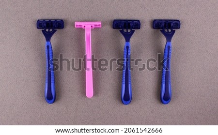 Three blue razors and one pink razor on a gray background. Gender concept