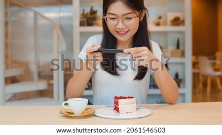 Blogger Asian friendly women influencer eat cake at night cafe. Beautiful young lady happy relax fun using technology mobile phone taking a photo of her food upload in social media at college campus.