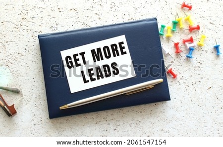Text GET MORE LEADS on a business card lying on a blue notebook next to the glasses. Business concept.