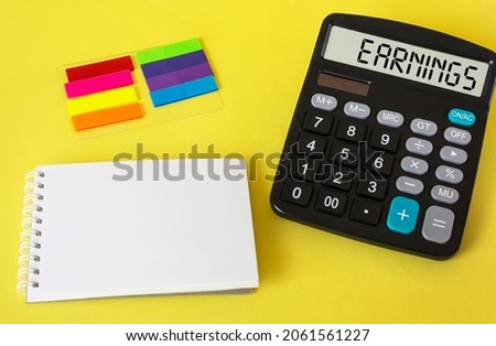 On a yellow background, a calculator with the phrase Earnings, next to a notepad for writing and stickers