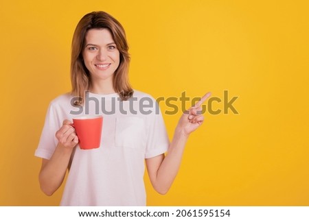 Photo of promoter lady hold red cup drink tea direct finger empty space wear casual t-shirt on yellow background