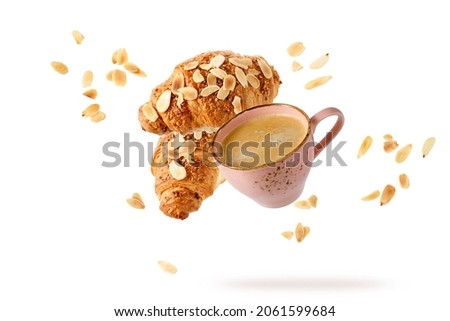Fresh baked almond  breakfast croissants  with nuts flakes crumbs, pink vintage cup of hot coffee  flying isolated on white. Two croissants and cup falling. Pastry shop or good morning cafe card
