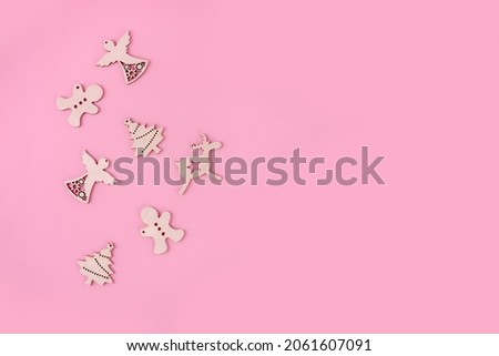 wooden figurines of Christmas angel, deer, spruce and gingerbread cookies on a pink background