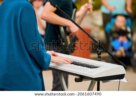 Musician woman playing on white synthesizer keyboard piano keys, focus on female hands on synthesizer. Musician playing musical instrument on concert stage, cropped image of person playing synthesizer Royalty-Free Stock Photo #2061607490