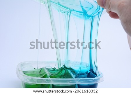 The hand unpacks a transparent container with new blue and green slides. On a uniform gray background