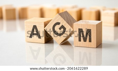 Three wooden cubes with the letters AGM on the bright surface of a gray table. the inscription on the cubes is reflected from the surface of the table. business concept. agm - annual general meeting Royalty-Free Stock Photo #2061622289