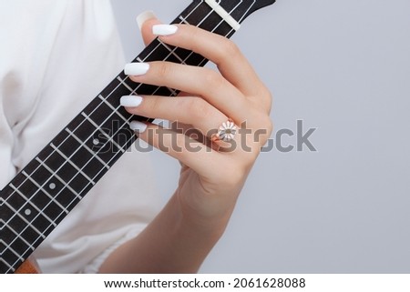 Girl playing the ukulele with a daisy ring in her hand