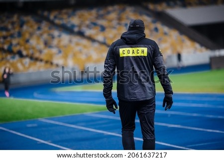 A man in dark sportswear at the stadium with the word Coach on the back Royalty-Free Stock Photo #2061637217