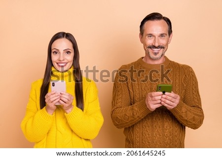 Photo of brunette optimistic couple look telephones wear knit sweaters isolated on beige background