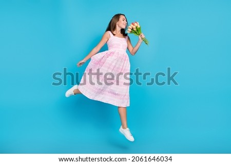 Full length photo of brown haired stylish attractive beautiful woman jump smell tulips isolated on blue color background