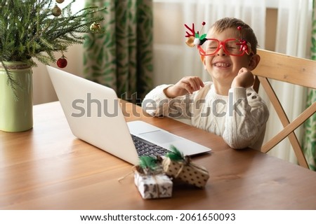  Little boy in a white sweater and funny glasses sits at a laptop and writes a letter to Santa Claus.