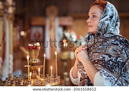 a young woman in a headscarf prays in an Orthodox church and puts candles in front of icons Royalty-Free Stock Photo #2061658652