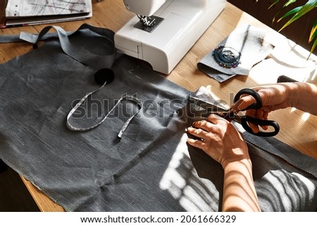 Woman cutting out a pattern paper in linen fabric. Seamstress sewing on the sewing machine in small studio. Fashion atelier, tailoring, handmade clothes concept. Slow Fashion Conscious consumption Royalty-Free Stock Photo #2061666329