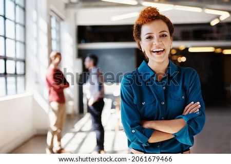 Portrait of a young businesswoman standing in an office with her colleagues in the background Royalty-Free Stock Photo #2061679466