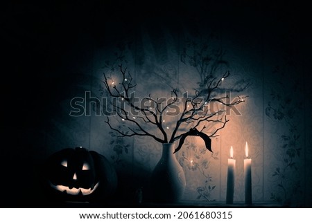 Halloween monotone picture with the Jack O'lantern, a bat, tree branches, two candles and dark shadows on the wall
